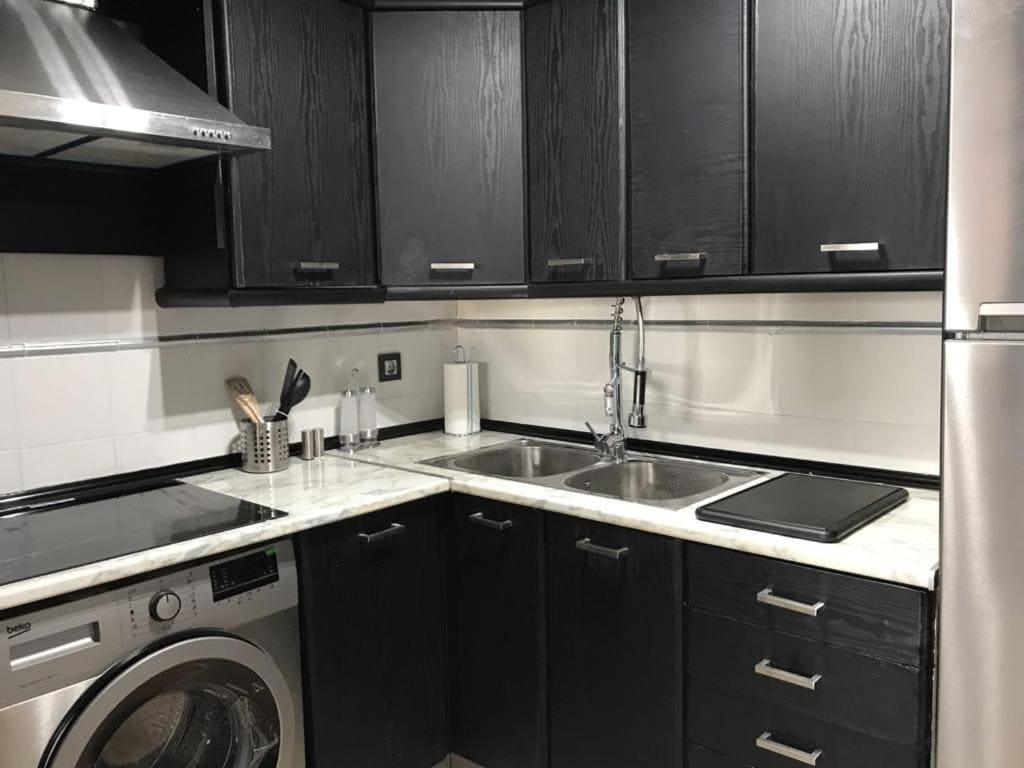 Modern black kitchen cabinets with white marble countertops in luxury Malaga apartment.