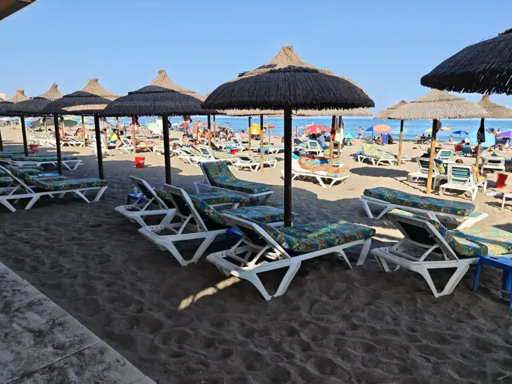 Sunbeds and straw parasols on the sandy shore at a chiringuito in Los Boliches, Málaga, Costa del Sol