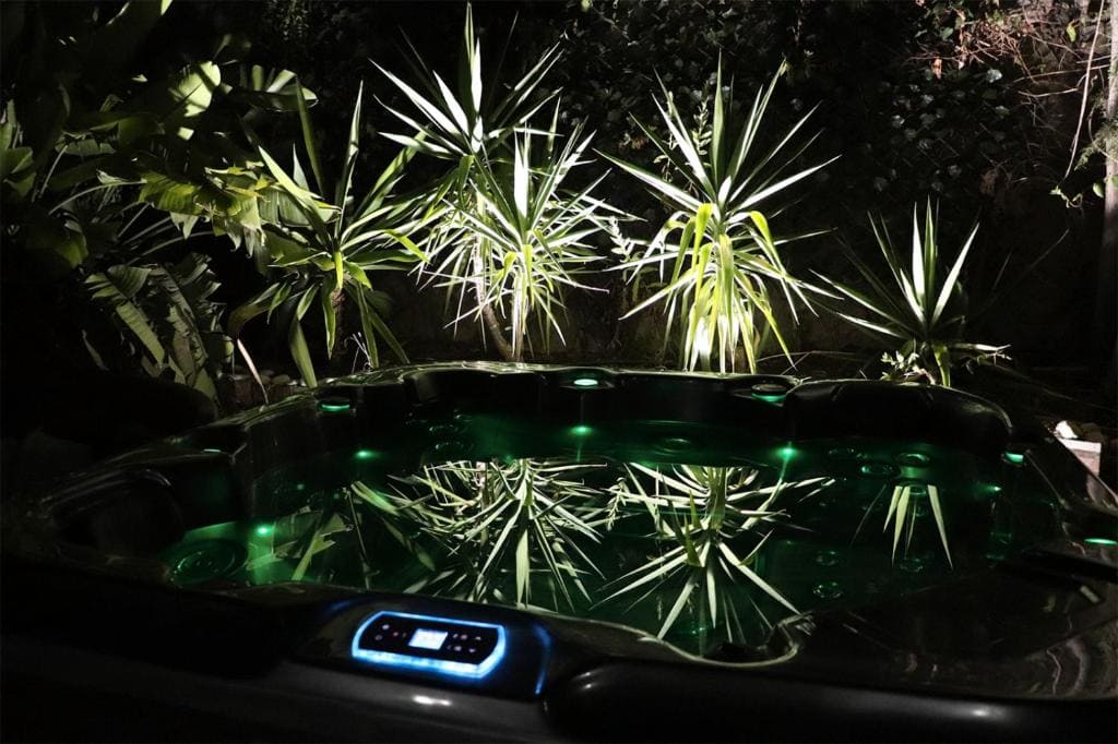 Luxurious hot tub with green LED lighting at night, surrounded by tropical plants in Malaga.