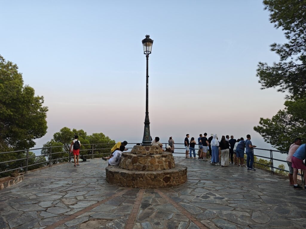 Things to do in Málaga Panoramic view from Mirador de Gibralfaro in Malaga, overlooking lush greenery and city scenery at sunset.